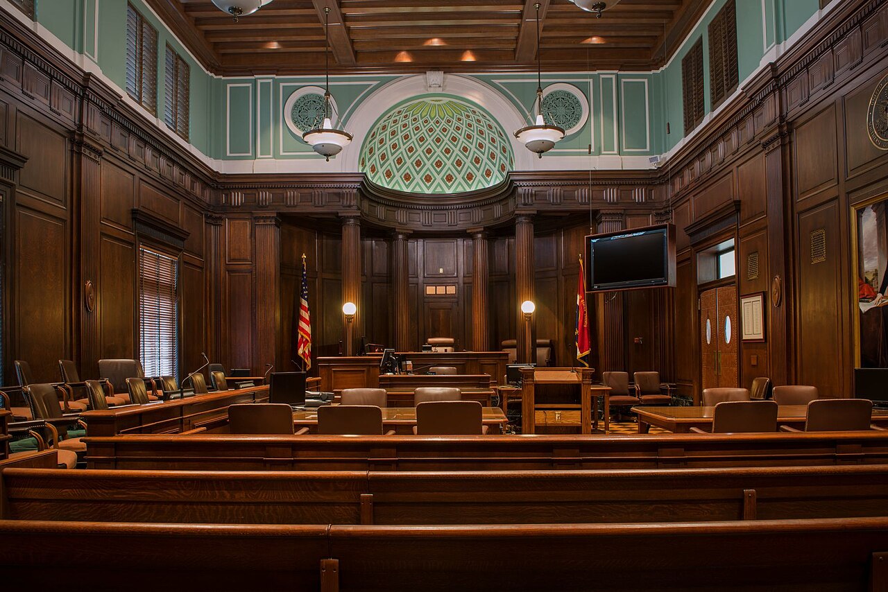An empty courtroom with wooden benches, a judge's bench, and a public gallery.